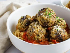 A white bowl filled with spaghetti, marinara sauce, and golden-brown eggplant meatballs topped with herbs and parmesan.