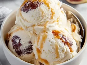 Two scoops of creamy fig ricotta ice cream in a white bowl, drizzled with caramel and topped with fig pieces.