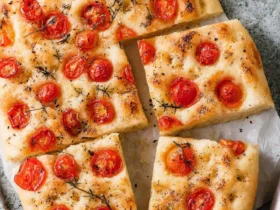 Freshly baked Focaccia with Tomatoes topped with roasted cherry tomatoes and herbs, sliced into pieces on parchment paper.