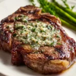 Juicy Garlic Butter Ribeye Steak topped with melted herb butter, served on a white plate with asparagus.