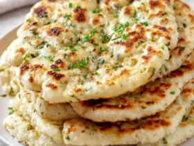 Stack of golden-brown Garlic Herb Flatbread topped with fresh herbs on a white plate.