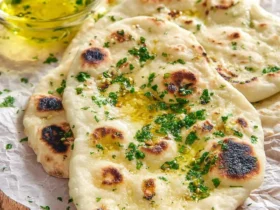 Freshly cooked Garlic Naan Bread topped with melted butter and chopped cilantro, served on parchment paper with garlic herb oil on the side.