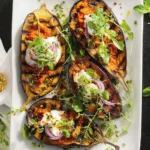 Grilled Eggplant with Harissa served on a white plate, topped with yogurt, red onion, and fresh herbs.