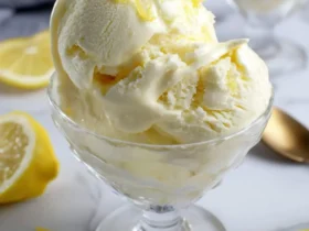 Two scoops of creamy lemon custard ice cream topped with fresh lemon zest in a glass dish.