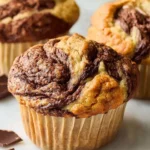 Close-up of freshly baked Nutella Banana Swirl Muffins with marbled chocolate tops in paper liners.