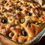 Golden baked Olive Rosemary Focaccia in a glass dish, topped with green and black olives and fresh rosemary sprigs.