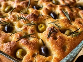 Golden baked Olive Rosemary Focaccia in a glass dish, topped with green and black olives and fresh rosemary sprigs.