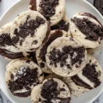 A white plate piled high with Oreo cheesecake cookies topped with chocolate cookie crumbles.
