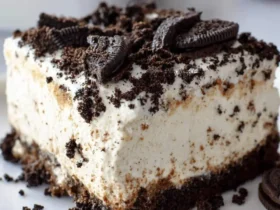 A slice of creamy Oreo Dirt Cake topped with crushed cookies and whole Oreos on a white plate.