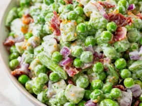 Creamy pea salad with bacon, red onion, and cheese in a white bowl on a marble surface.