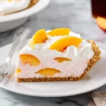 A slice of Peach Cool Whip Pie with graham cracker crust, creamy filling with peach slices, and whipped topping on a white plate.