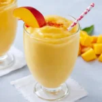 Creamy Peach Mango Smoothie in a glass with a peach slice and striped straw.