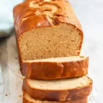A freshly baked loaf of peanut butter bread with three slices cut and stacked in front, showing a soft, moist crumb.