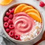 Raspberry Orange Smoothies Recipes Bowl topped with fresh orange slices, raspberries, coconut flakes, and granola in a ceramic bowl.