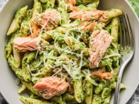 Salmon Pesto Pasta 55 A bowl of salmon pesto pasta with penne, flaky salmon pieces, green basil pesto, and grated parmesan cheese.