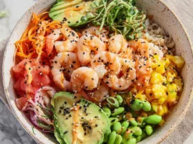 A vibrant Shrimp Poke Bowl with fresh avocado, edamame, corn, carrots, and sesame seeds over rice.