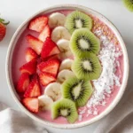 A colorful Strawberry Kiwi Smoothies Recipes Bowl topped with fresh sliced strawberries, bananas, kiwi, coconut flakes, and granola.