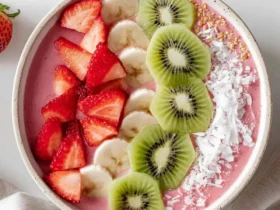 A colorful Strawberry Kiwi Smoothies Recipes Bowl topped with fresh sliced strawberries, bananas, kiwi, coconut flakes, and granola.
