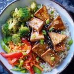 Teriyaki Tofu Bowl with crispy tofu, broccoli, vegetables, and rice topped with sesame seeds and green onions.