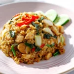 A plate of Thai basil chicken fried rice topped with red chili slices and served with cucumber.