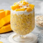 Tropical Mango Overnight Oats served in a glass with fresh mango chunks and coconut flakes on top.