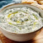 Creamy Tzatziki Sauce in a rustic bowl, garnished with olive oil and fresh dill, served with pita bread.