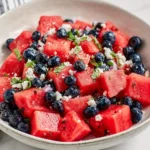 Fresh watermelon blueberry salad with feta cheese, mint, and red onion in a white bowl on a marble surface.