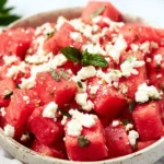 Fresh Watermelon Feta Salad with mint in a speckled ceramic bowl, featuring cubed watermelon and crumbled feta cheese.