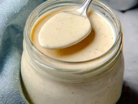 Alabama White BBQ Sauce 42 A spoonful of creamy Alabama White BBQ Sauce resting on a glass jar filled with the tangy, mayonnaise-based condiment.