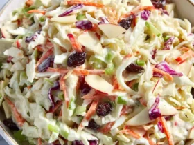 Creamy apple coleslaw with shredded cabbage, carrots, sliced almonds, and dried cranberries in a bowl.