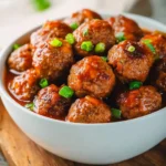 A white bowl filled with glazed BBQ Meatballs Crockpot style, topped with fresh green onions on a wooden surface.
