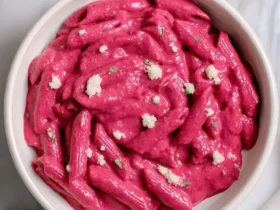 A bowl of penne pasta coated in creamy vibrant pink Beetroot Pasta Sauce, topped with cheese and herbs.