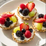 Four colorful Breakfast Fruit Tarts with granola crusts, yogurt filling, and fresh berries arranged on a white plate.