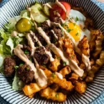 Burger Bowls with House Sauce and Ranch Fries topped with a fried egg, lettuce, pickles, and drizzled sauce in a striped bowl.