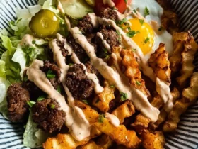 Burger Bowls with House Sauce and Ranch Fries topped with a fried egg, lettuce, pickles, and drizzled sauce in a striped bowl.