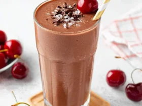 A tall glass of cherry chocolate smoothie topped with chocolate shavings, sea salt, and a fresh cherry.