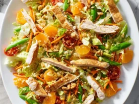 A colorful chinese chicken salad with mandarin oranges, snap peas, chicken strips, and crispy wontons in a white bowl.