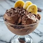 Chocolate Banana Greek Frozen Yogurt topped with chocolate shavings and fresh banana slices in a glass bowl.
