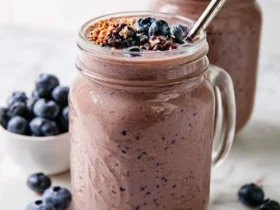 Two mason jars filled with chocolate berry smoothie topped with fresh blueberries and granola, with a metal straw.