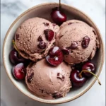 Three scoops of Chocolate Cherry Ice Cream in a ceramic bowl topped with fresh cherries.