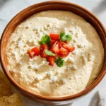 Creamy Cottage Cheese Queso Dip topped with fresh tomatoes, cilantro, and crumbled cheese in a brown ceramic bowl.