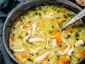 Greek Lemon Chicken Soup 49 A rustic bowl of Greek Lemon Chicken Soup with shredded chicken, carrots, dill, and a lemon slice floating in golden broth.
