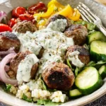 Greek Meatball Bowl with Tzatziki featuring grilled meatballs, fresh vegetables, and creamy herb sauce over rice.