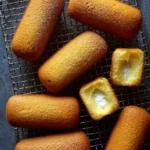 Golden homemade Twinkies with creamy filling rest on a cooling rack, two cut open to reveal the fluffy interior.