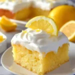 A slice of Lemon Poke Cake topped with whipped cream and a fresh lemon slice on a white plate.