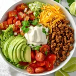 A colorful low carb burrito bowl filled with seasoned ground beef, fresh vegetables, avocado, cheese, and sour cream in a white bowl.
