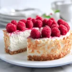 A sliced Low Carb Raspberry Cheesecake topped with fresh raspberries and toasted coconut on a white plate.