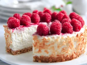 A sliced Low Carb Raspberry Cheesecake topped with fresh raspberries and toasted coconut on a white plate.