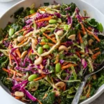 A large white bowl filled with colorful Miso Crunch Salad featuring kale, purple cabbage, carrots, edamame, and cashews.