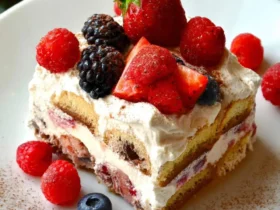 A slice of No-Bake Berry Tiramisu topped with fresh strawberries, raspberries, blackberries, and blueberries on a white plate.